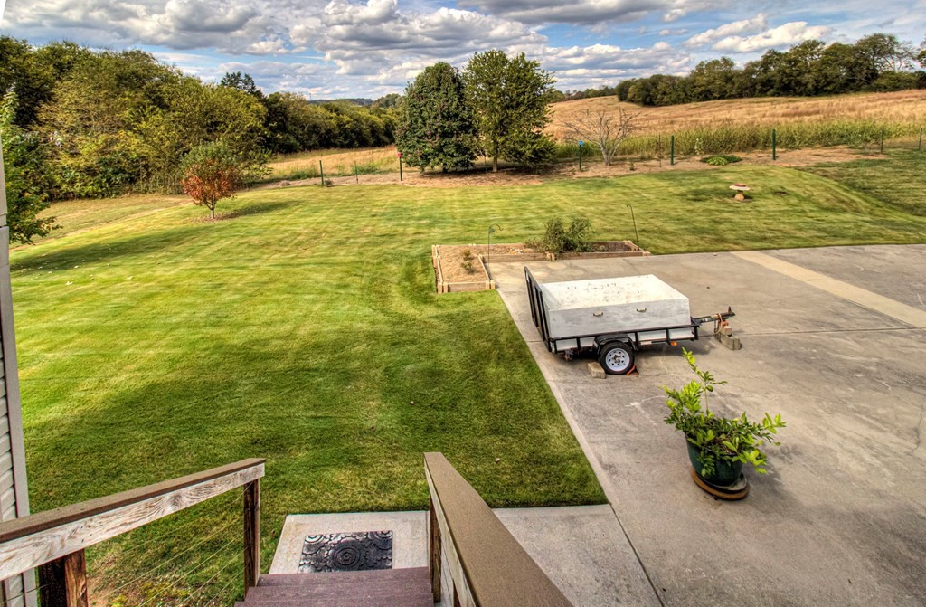 Broad lawn beside a concrete patio, with raised beds and open fields beyond.