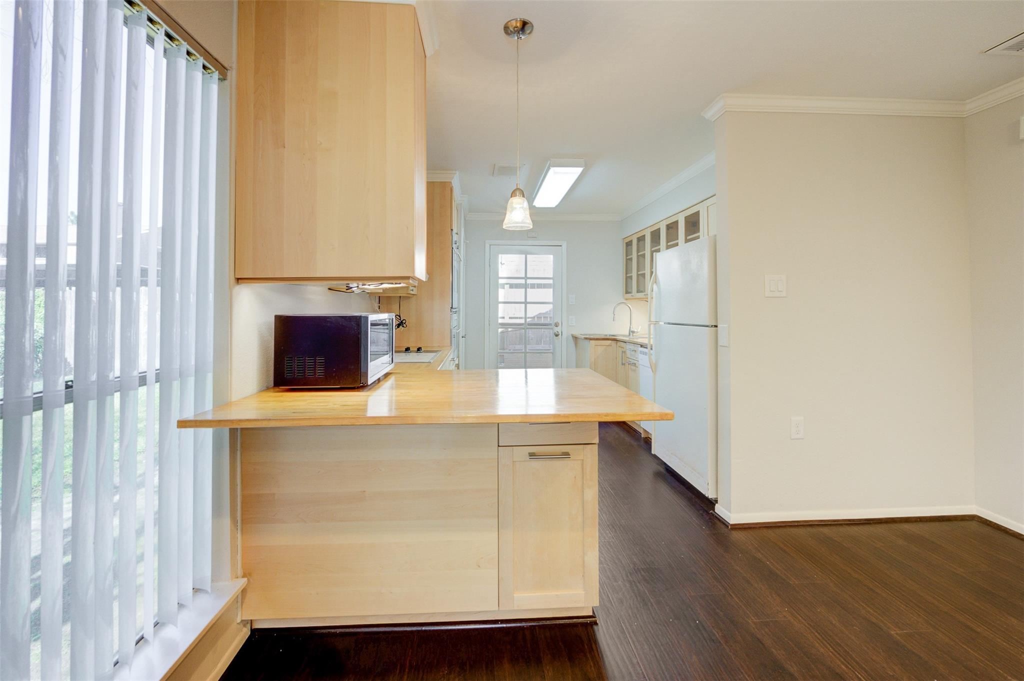 Kitchen with a wide wood-topped island, light wood cabinets, and dark flooring.