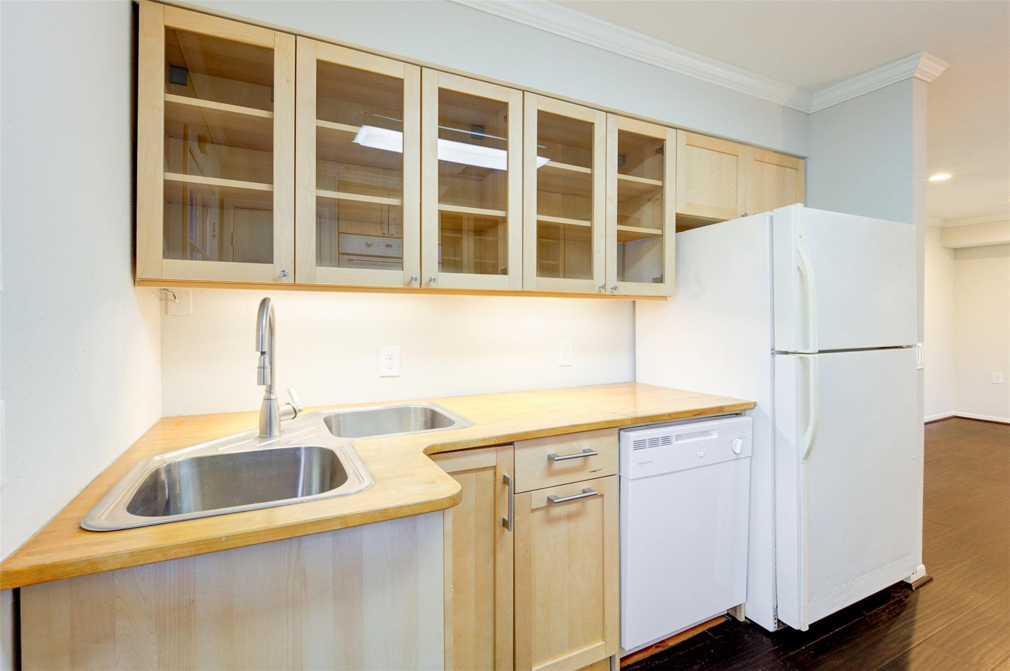 Kitchen with pale wood counters, glass-front cabinets, double sink, and white appliances.