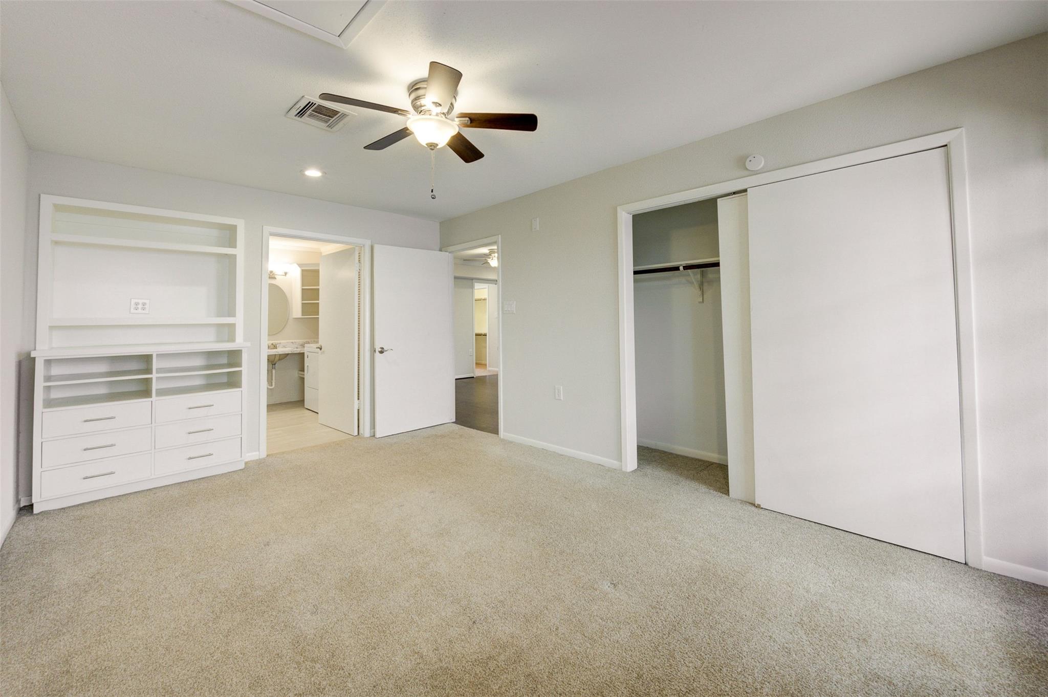 Empty carpeted bedroom with built-in shelving, a ceiling fan, and an open closet.