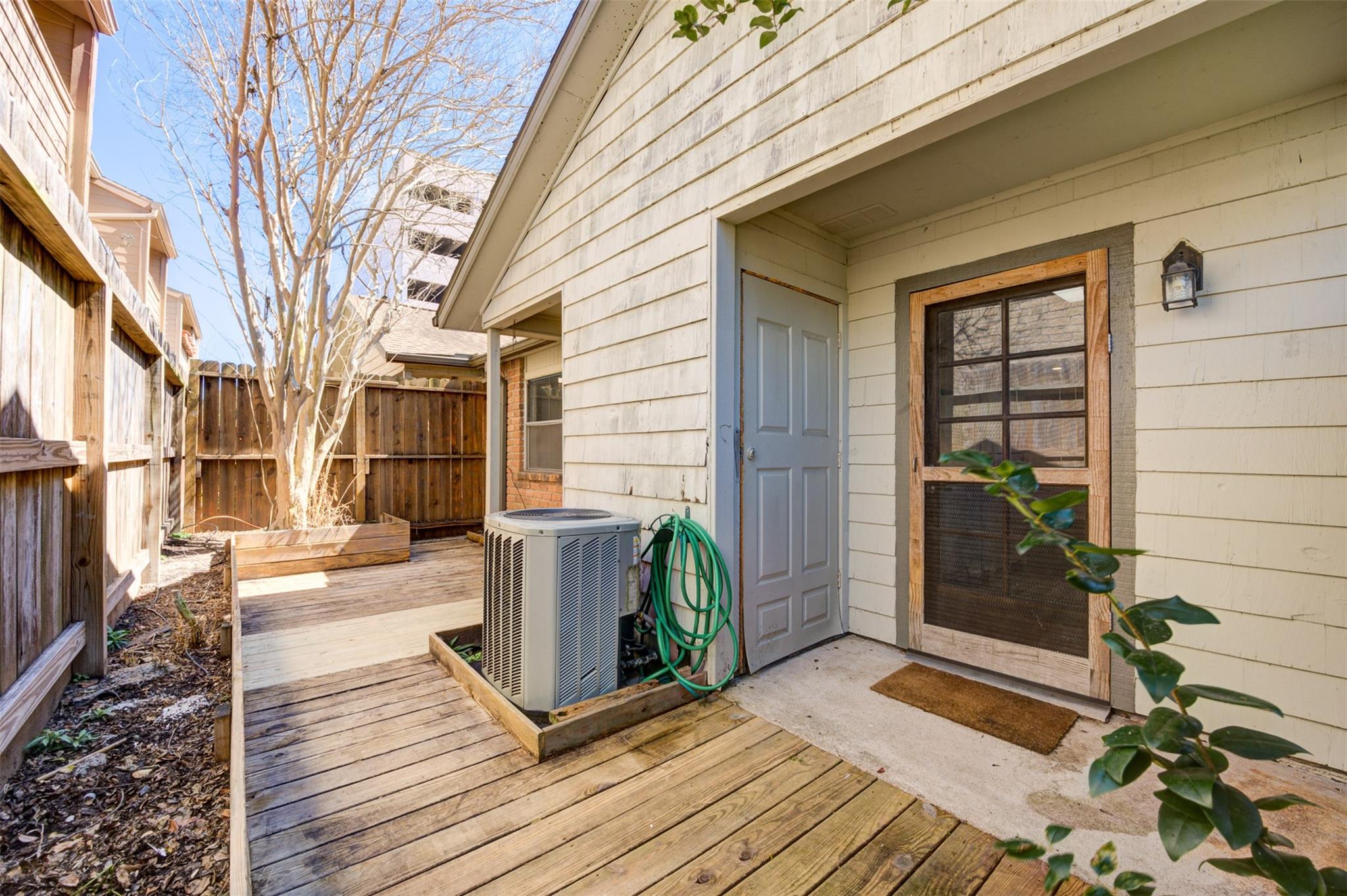 Fenced wooden deck and walkway beside the home, with a raised planter and side entrance.