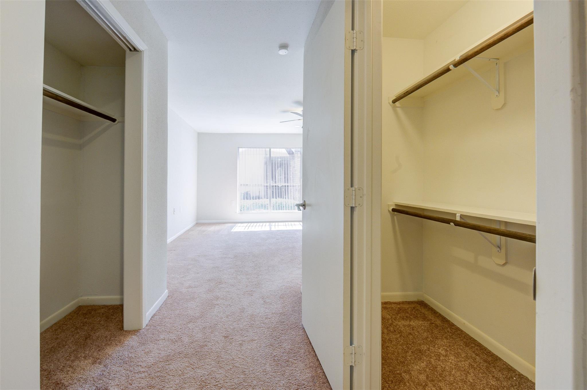 Two carpeted closets with hanging rods frame a bright, empty bedroom.