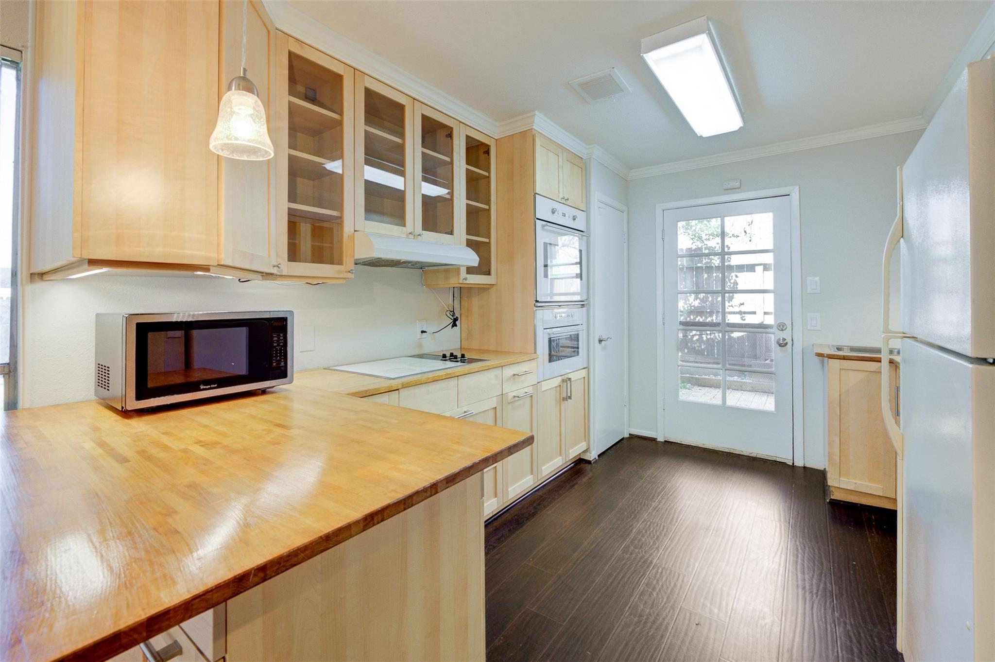 Kitchen with maple cabinetry, broad wood countertop, built-in double ovens, and a glazed exterior door.