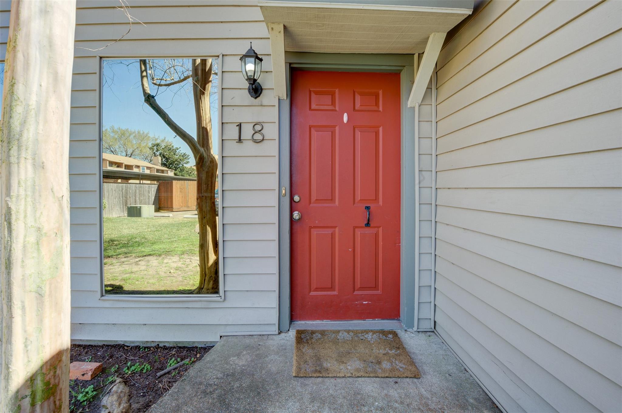 Home entrance with a red front door, unit number 18, and large window reflecting a tree.