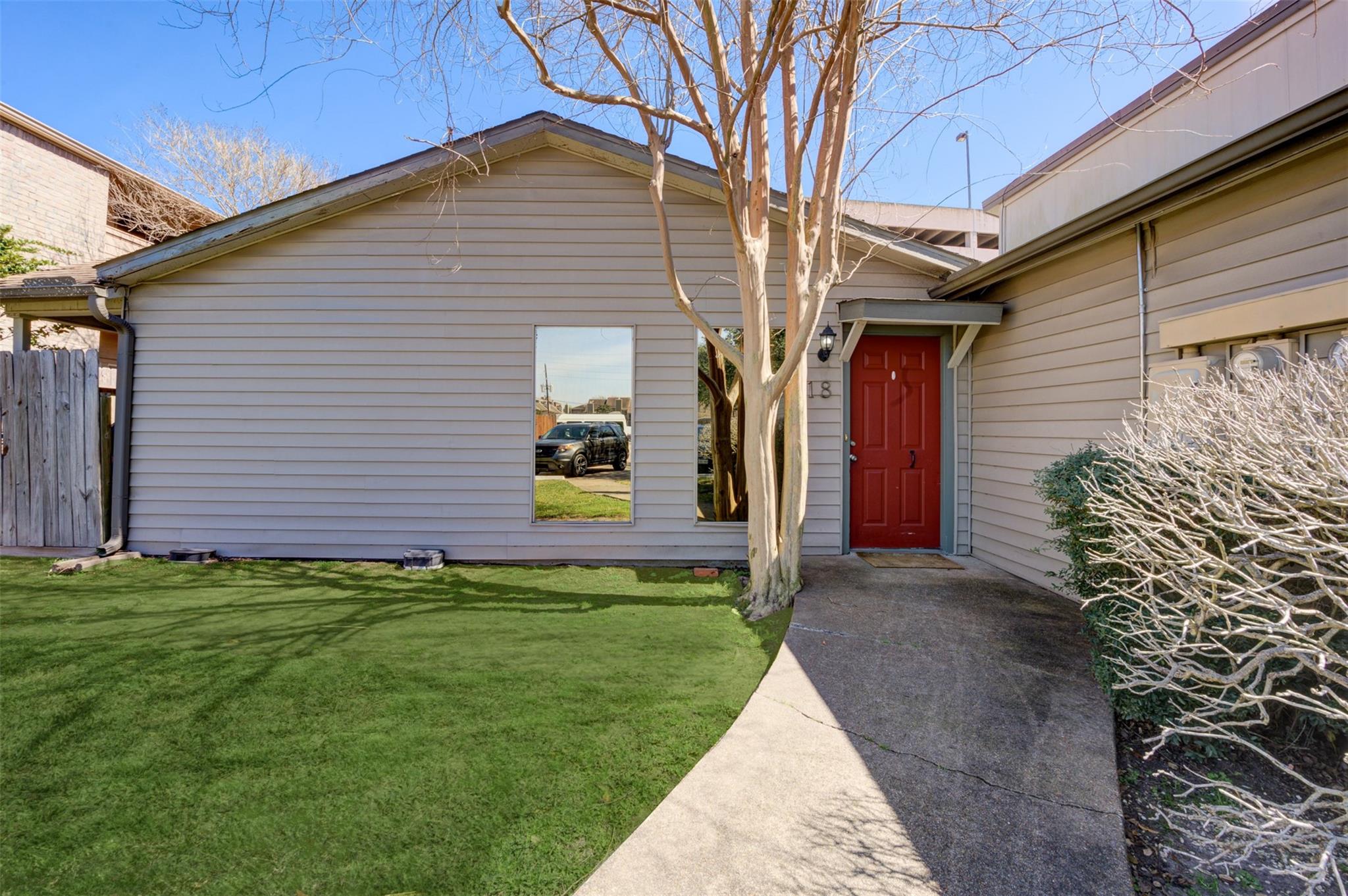 Gray-sided home with a red front door marked 18, a curved walkway, and a lawn beneath a leafless tree.