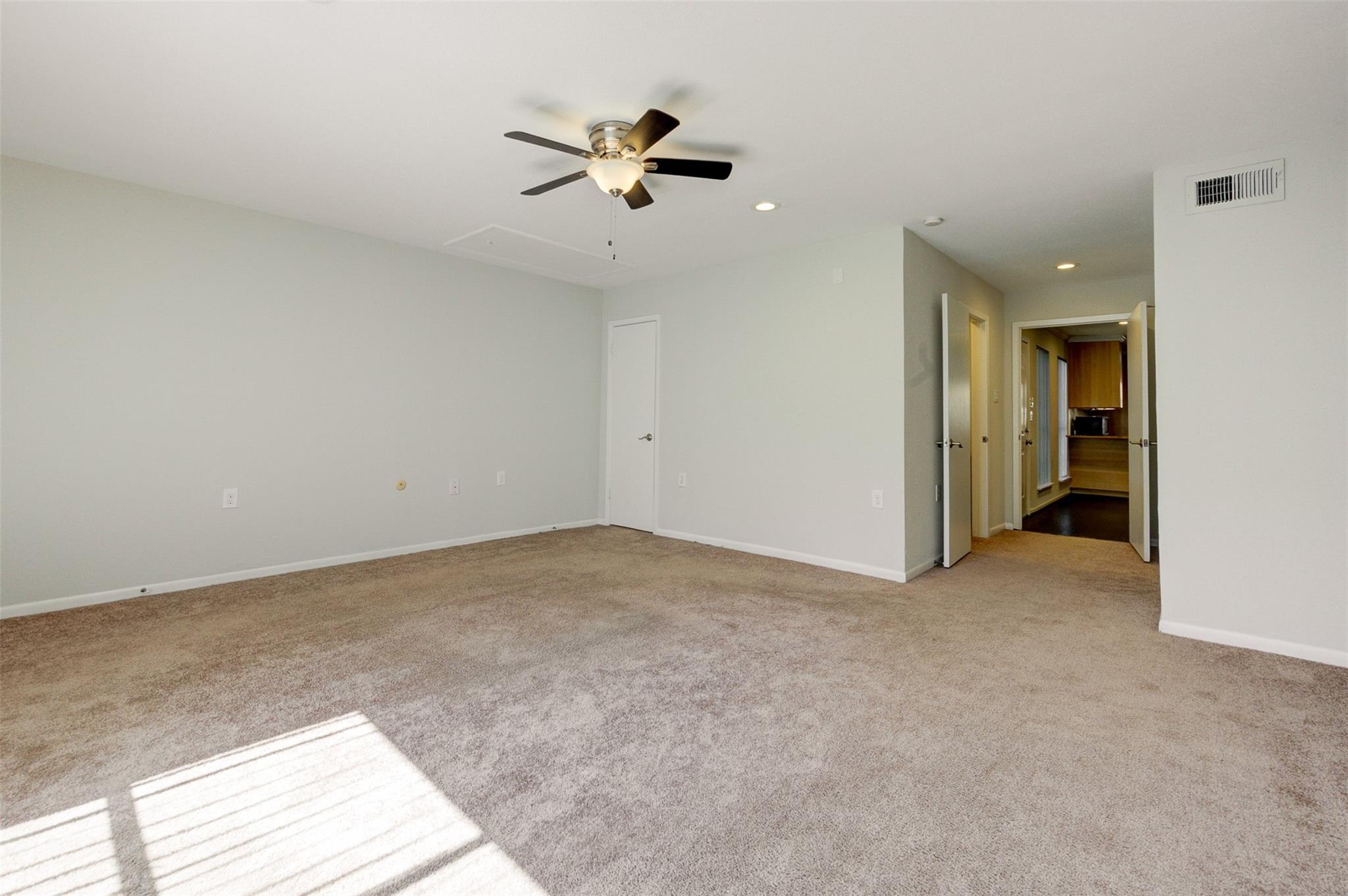 Empty carpeted bedroom with a ceiling fan and sunlight across the floor.