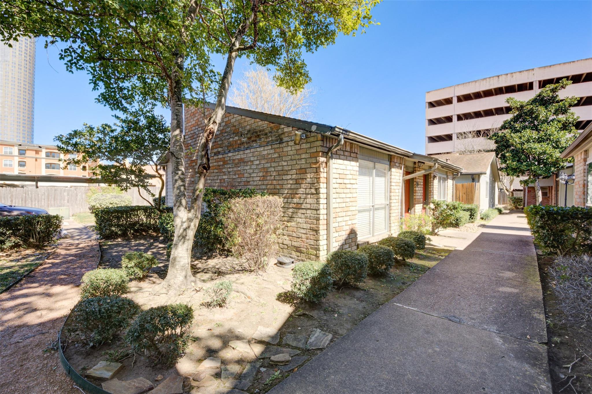 Brick townhouse beside a landscaped walkway shaded by mature trees.