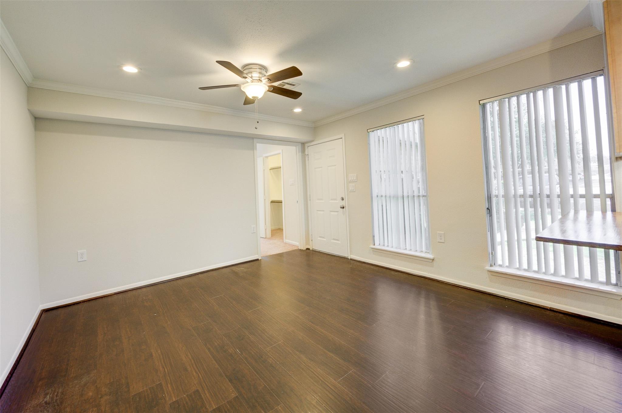 Vacant living area with dark flooring, a ceiling fan, and windows with vertical blinds.