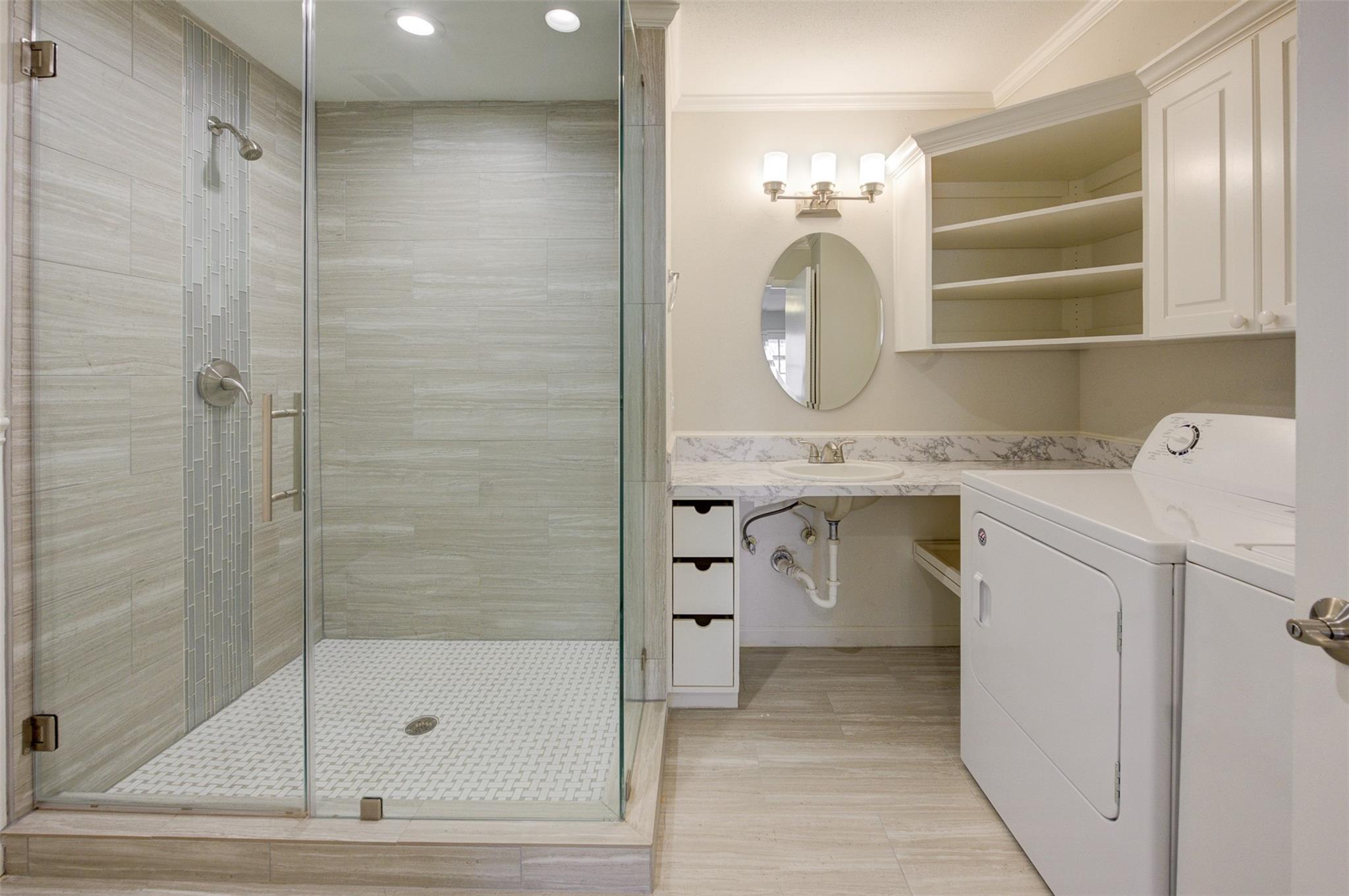 Bathroom with a glass-enclosed tiled shower, vanity, and washer and dryer.