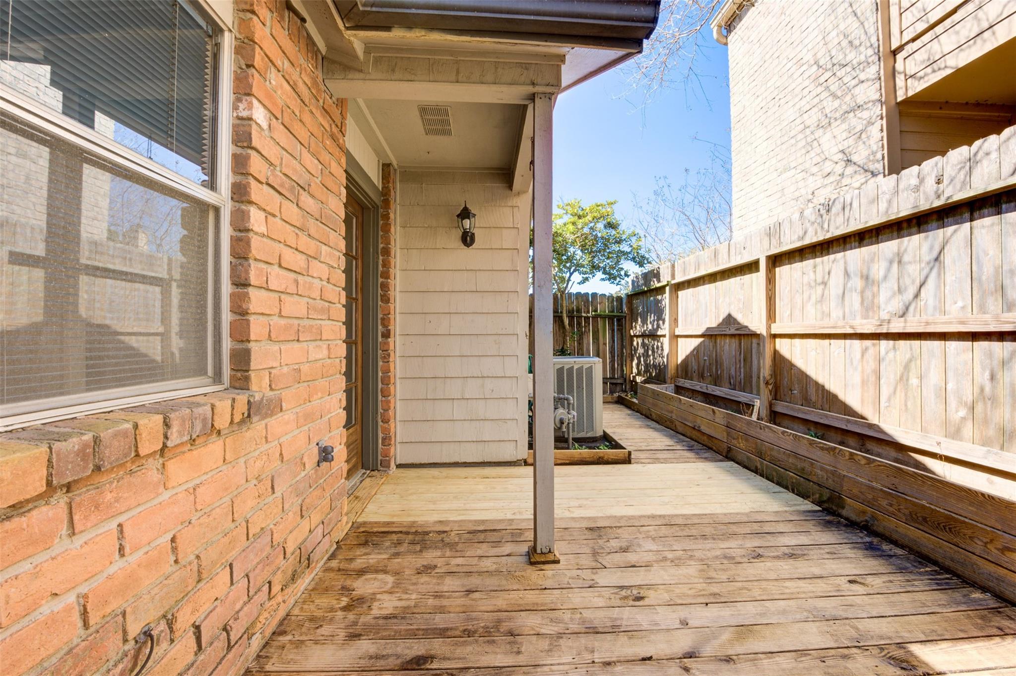 Wooden side deck beside a brick townhouse, enclosed by a tall privacy fence and raised planters.