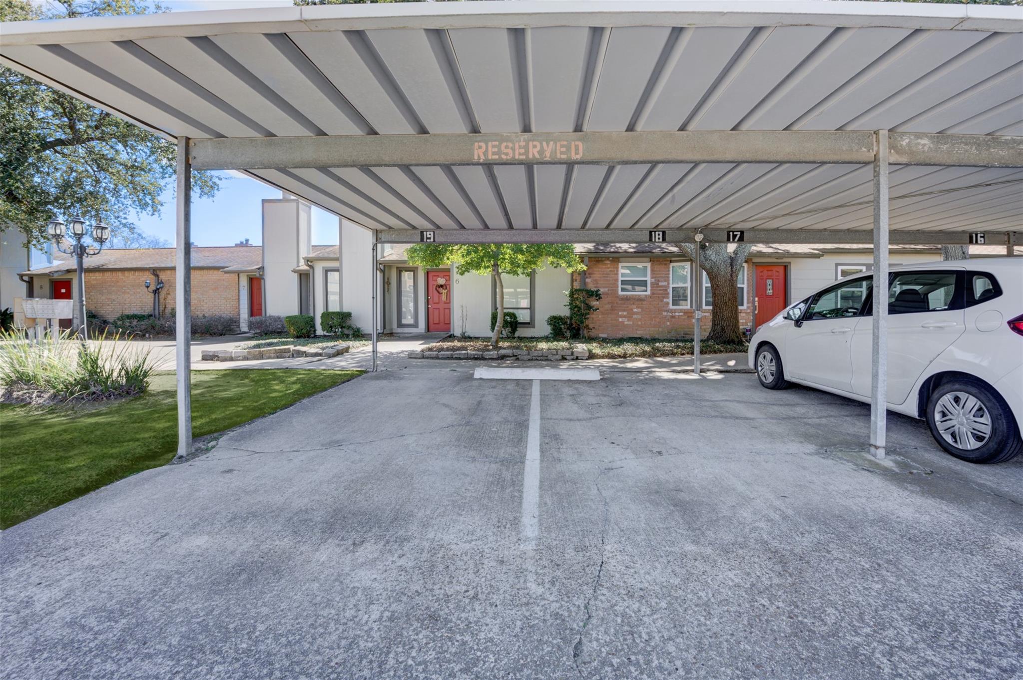 Covered reserved parking in front of townhomes, with numbered spaces and a white car.