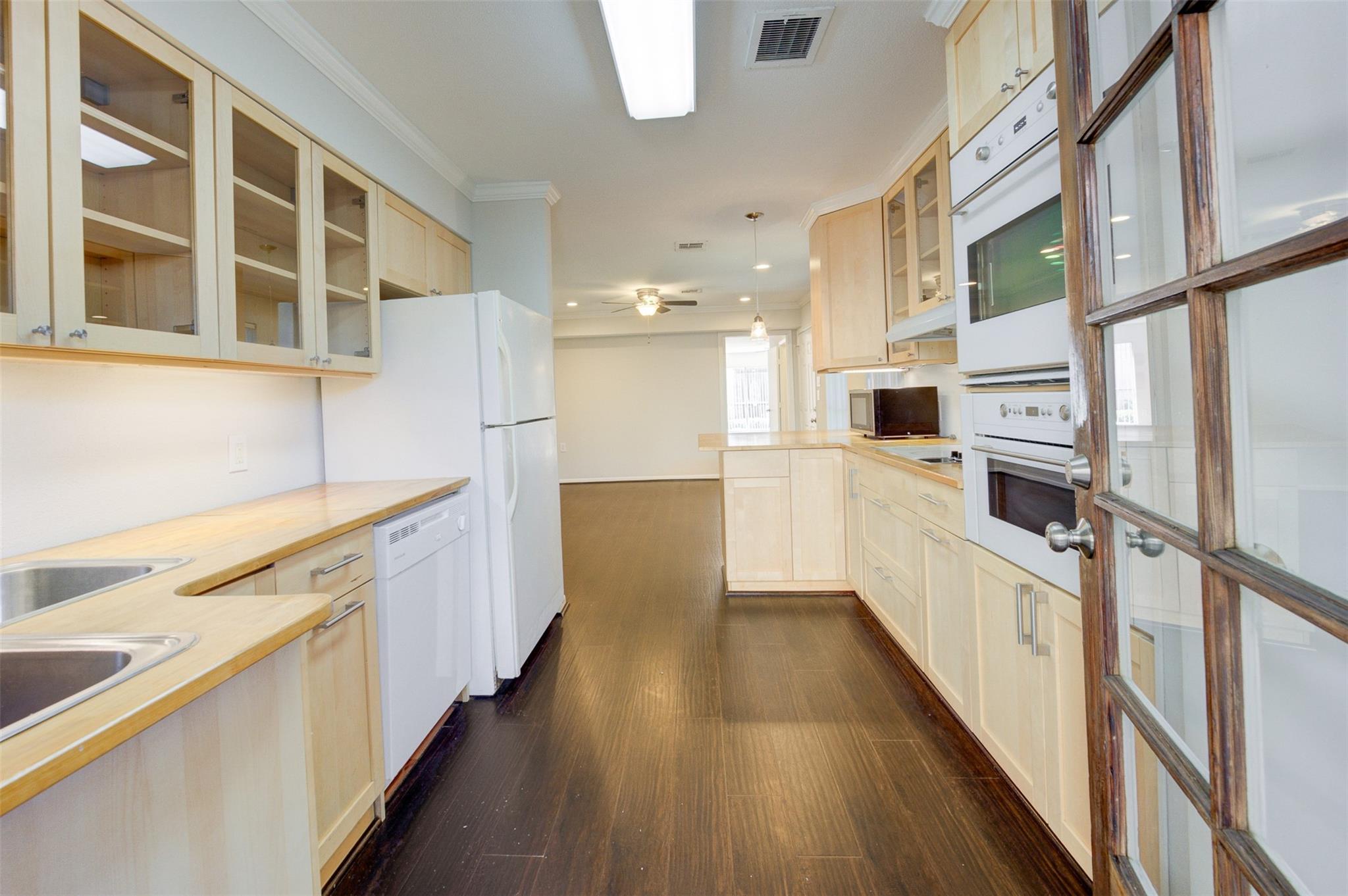 Vacant galley kitchen with pale wood cabinets, dark flooring, and built-in wall ovens.