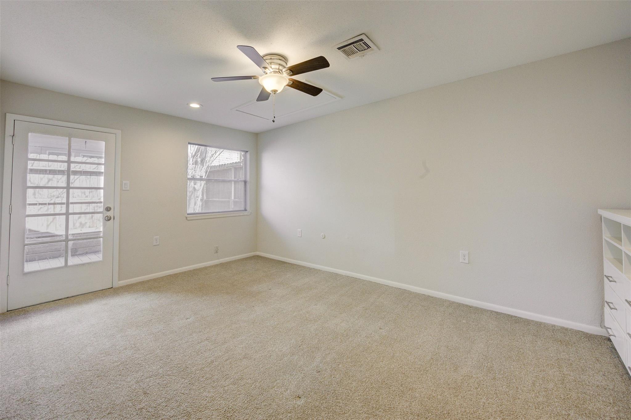 Empty carpeted room with a ceiling fan, window blinds, and a glass-paneled patio door.