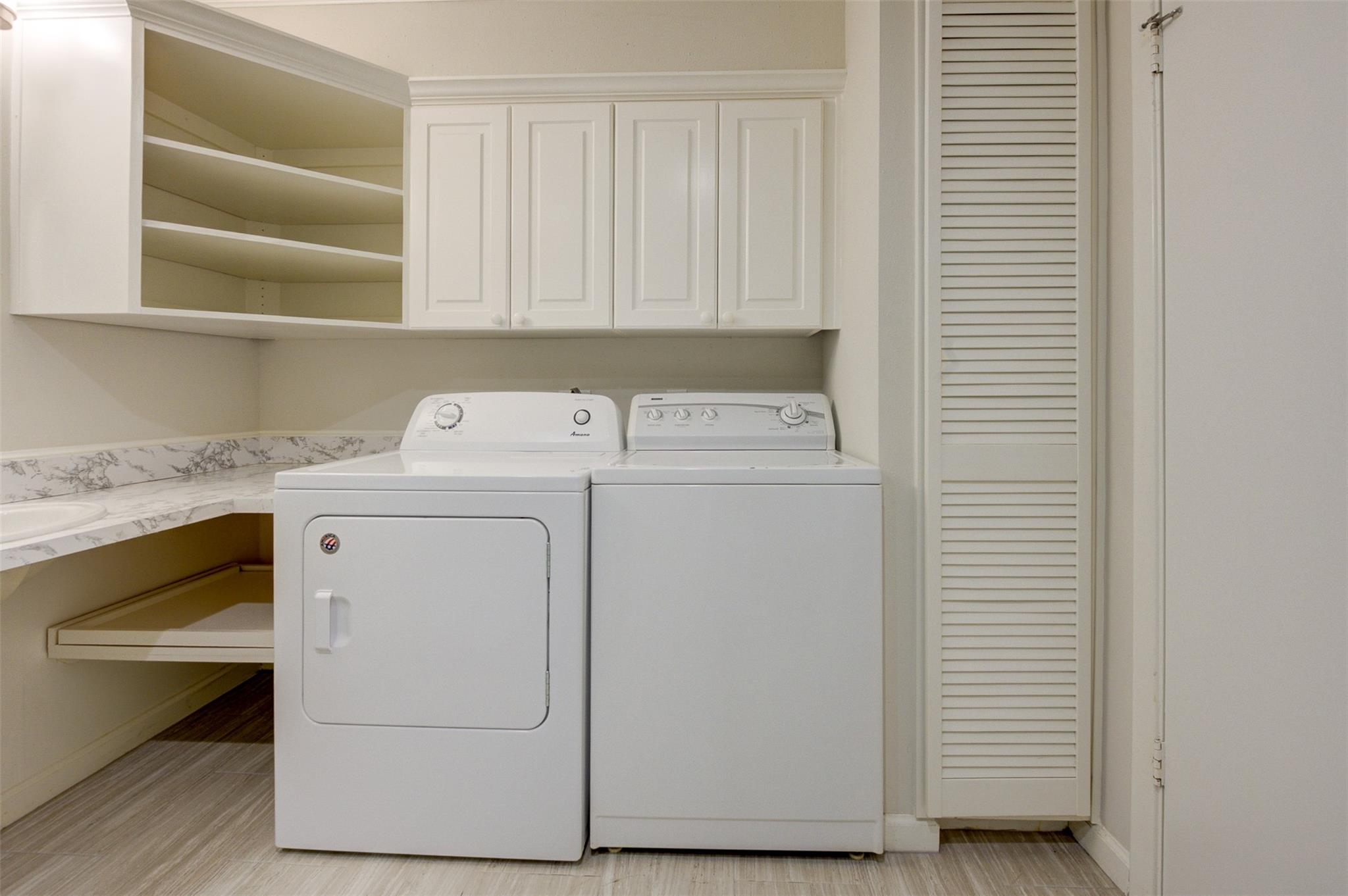 Laundry room with white washer and dryer, upper cabinets, and a countertop sink.