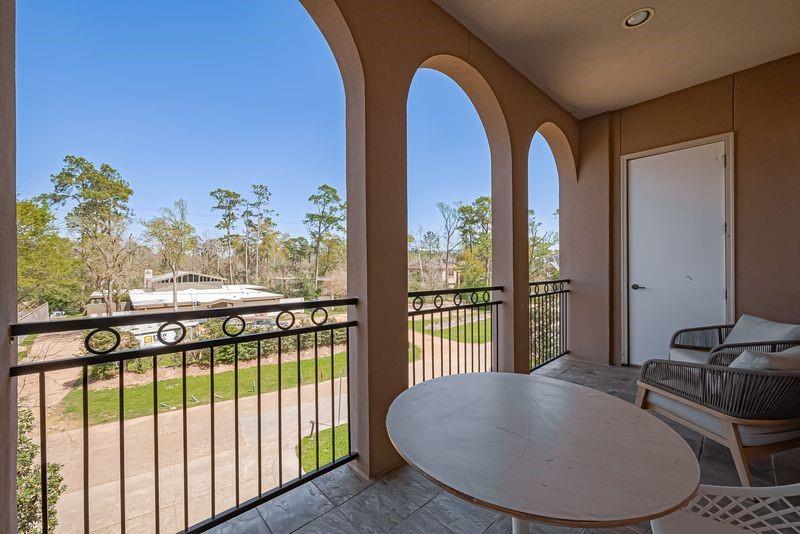 Covered balcony with arched openings, a round table, and a view of trees.