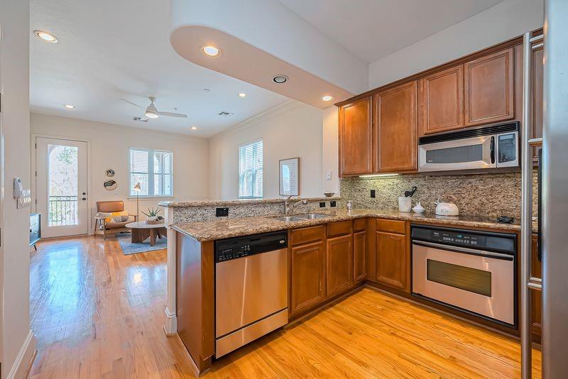 Open-plan kitchen with granite counters, wood cabinets, and stainless steel appliances beside a sitting area.