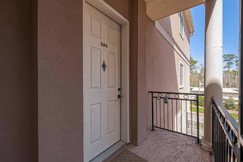 Condominium entry balcony with unit 303’s door, black railing, and neighboring building.