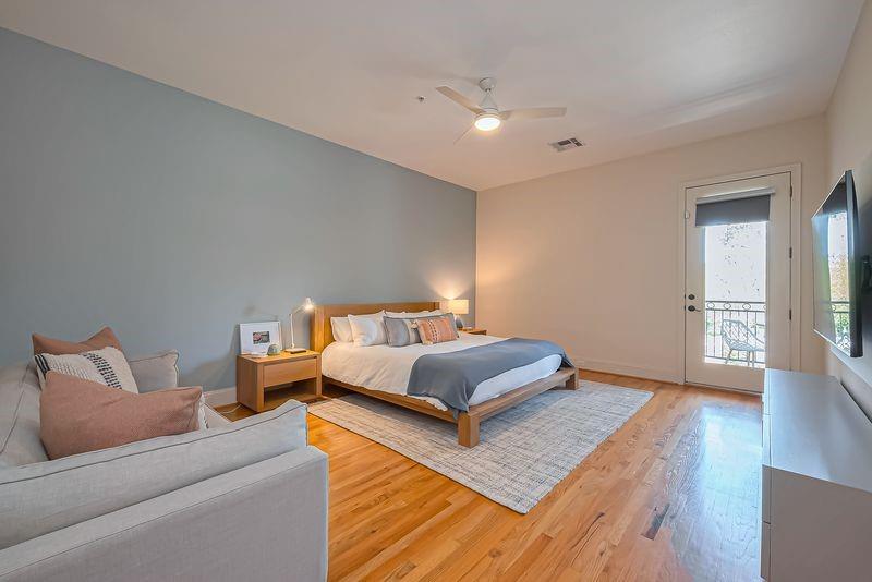 Staged bedroom with a wood-framed bed, pale sofa, and glass door to a balcony.
