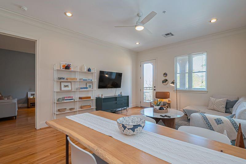 Open-plan living room and dining area with wood floors, wall shelving, and a balcony door.
