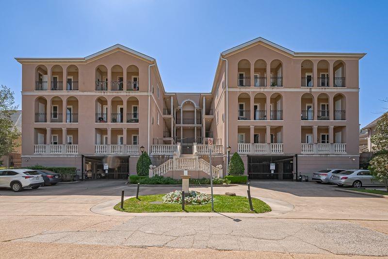 Condominium building with arched balconies and a central stairway, viewed from the parking area.