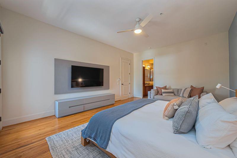 Furnished bedroom with a large white bed, blue throw, gray seating, and wall-mounted television.