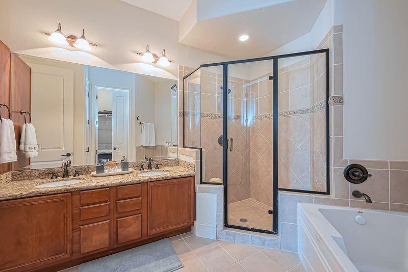 Bathroom with a double-sink wood vanity, glass-enclosed tiled shower, and built-in tub.