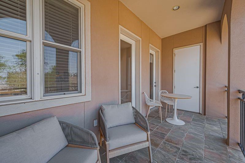 Covered balcony with cushioned chairs, tiled floor, and a small white table.
