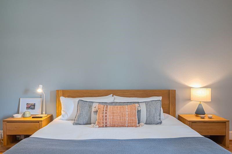 Bedroom with a wood headboard, gray and rust pillows, and matching bedside tables.