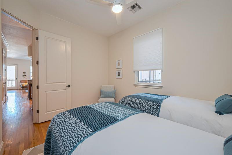 Bedroom with two beds, blue patterned throws, a small chair, and a window with a lowered blind.