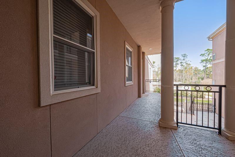 Covered apartment balcony with round columns and a black railing overlooking trees.