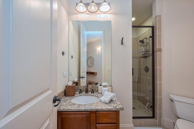 Bathroom with granite vanity, wood cabinetry, and a tiled glass-enclosed shower.