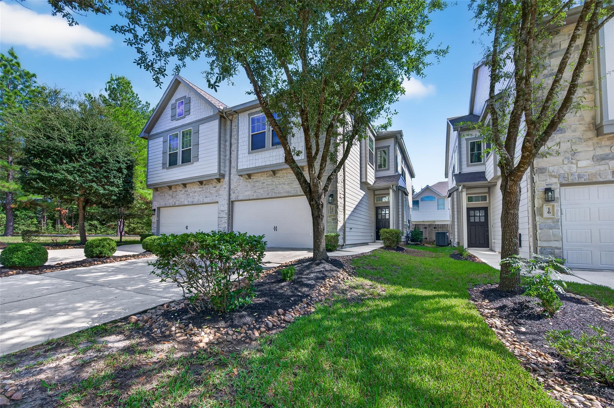 Light-sided townhomes with stone façades and garages, framed by mature trees and landscaped lawns.