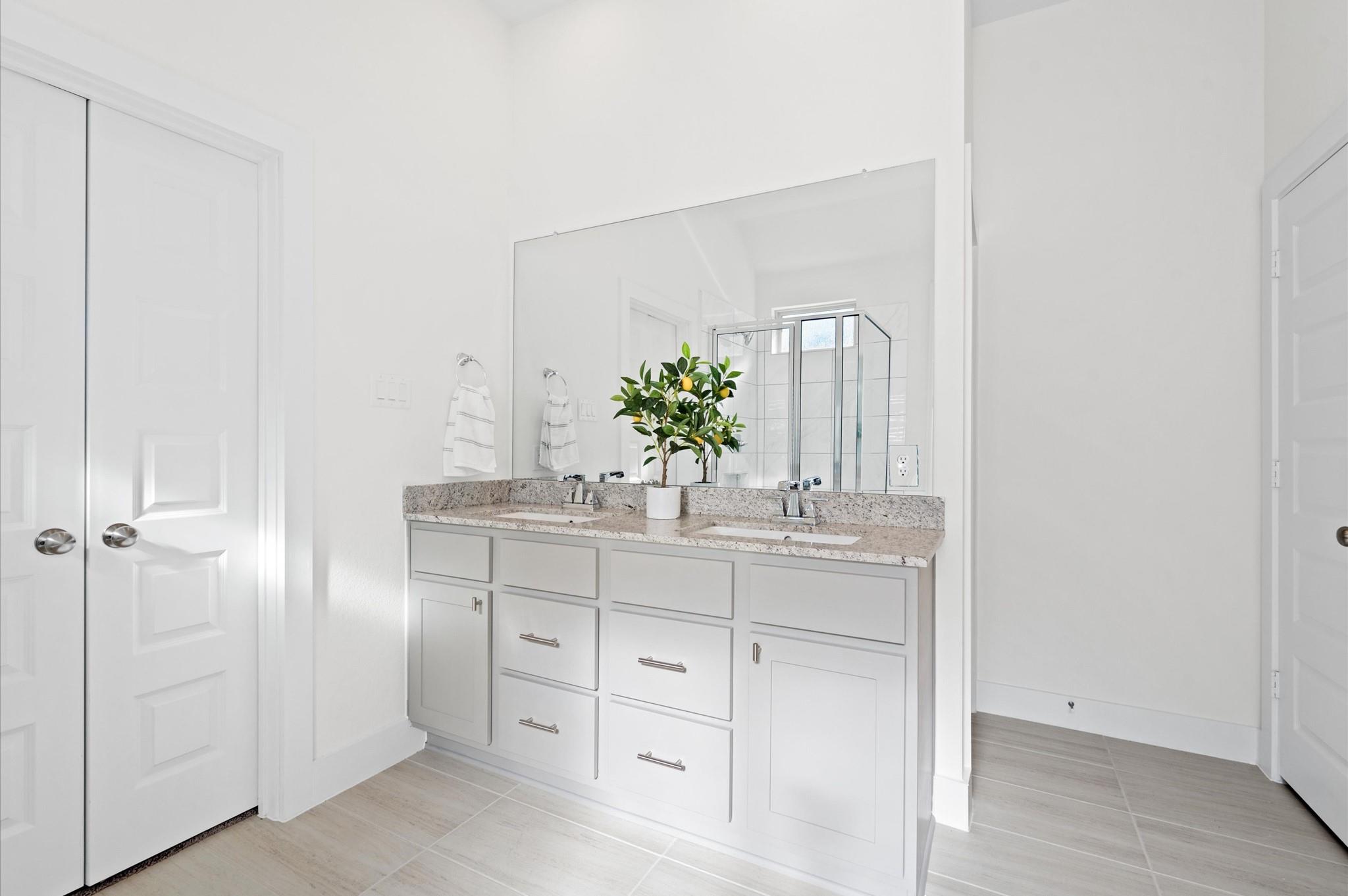 Bright bathroom with a white double vanity, speckled countertop, large mirror, and glass shower.