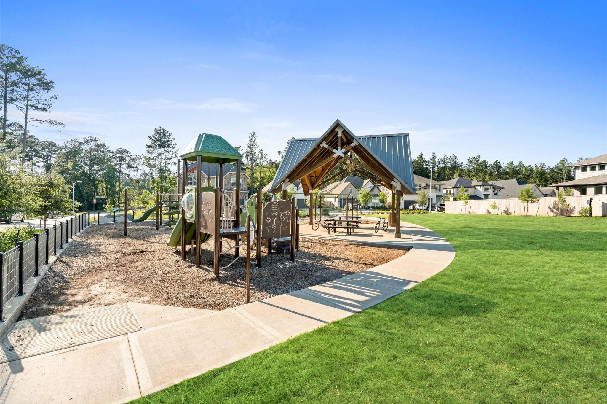 Neighborhood playground with a green-roofed play structure and a covered picnic pavilion beside a broad lawn.