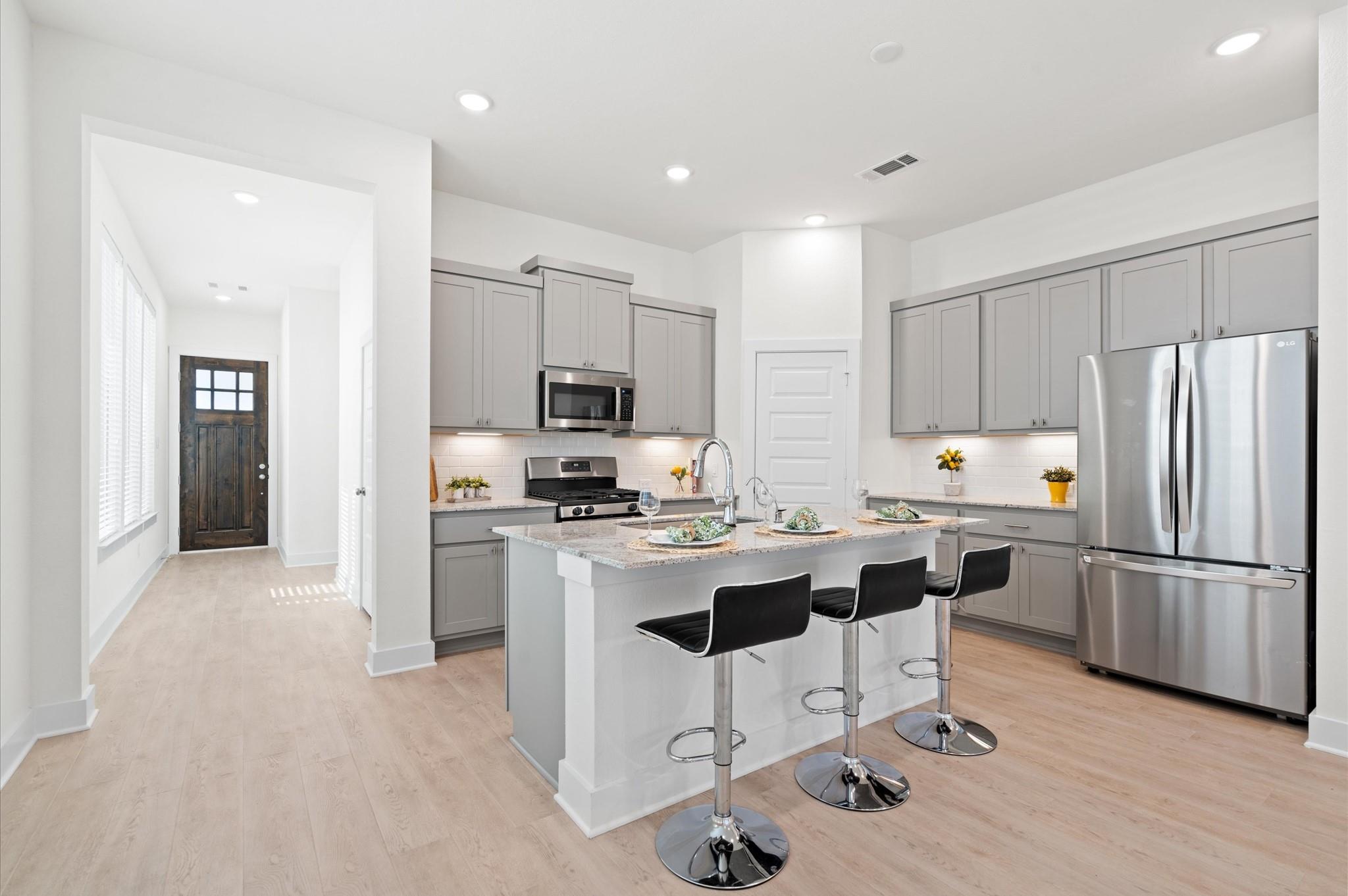 Kitchen with a large island, gray cabinets, stainless steel appliances, and three black bar stools.