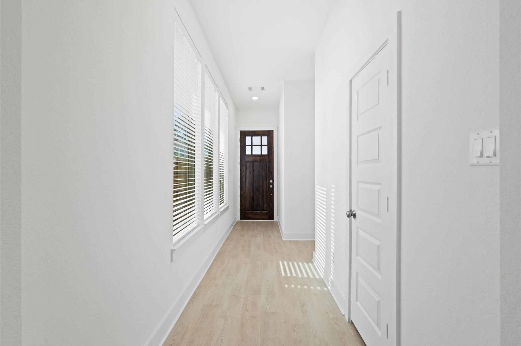 Entry hallway with tall blinded windows, light flooring, and a dark wood front door.