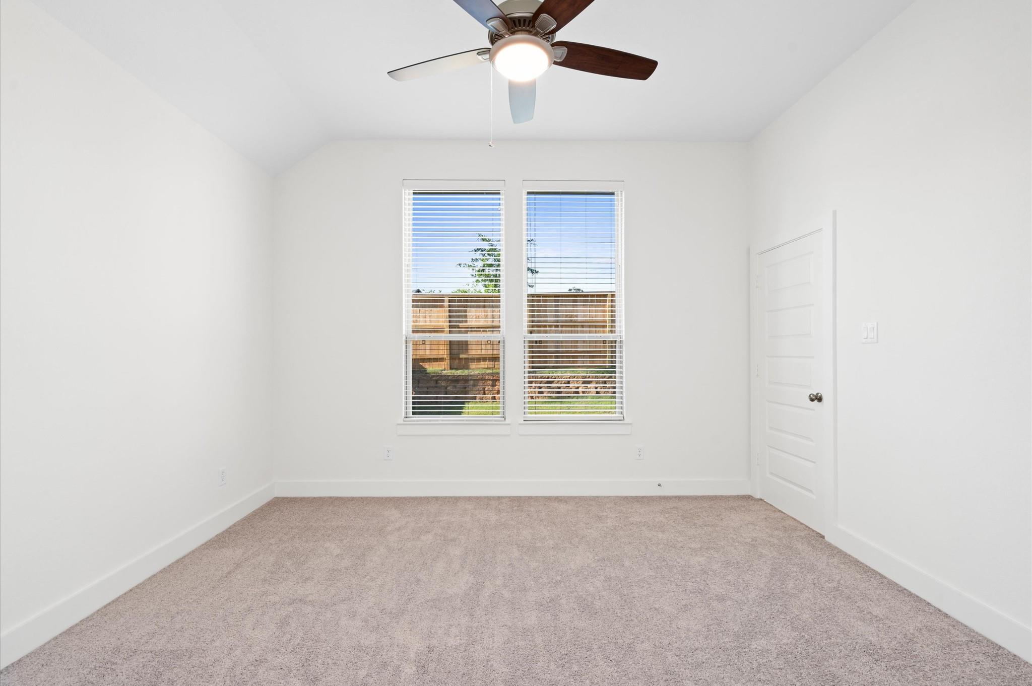 Empty carpeted bedroom with two blind-covered windows and a ceiling fan.