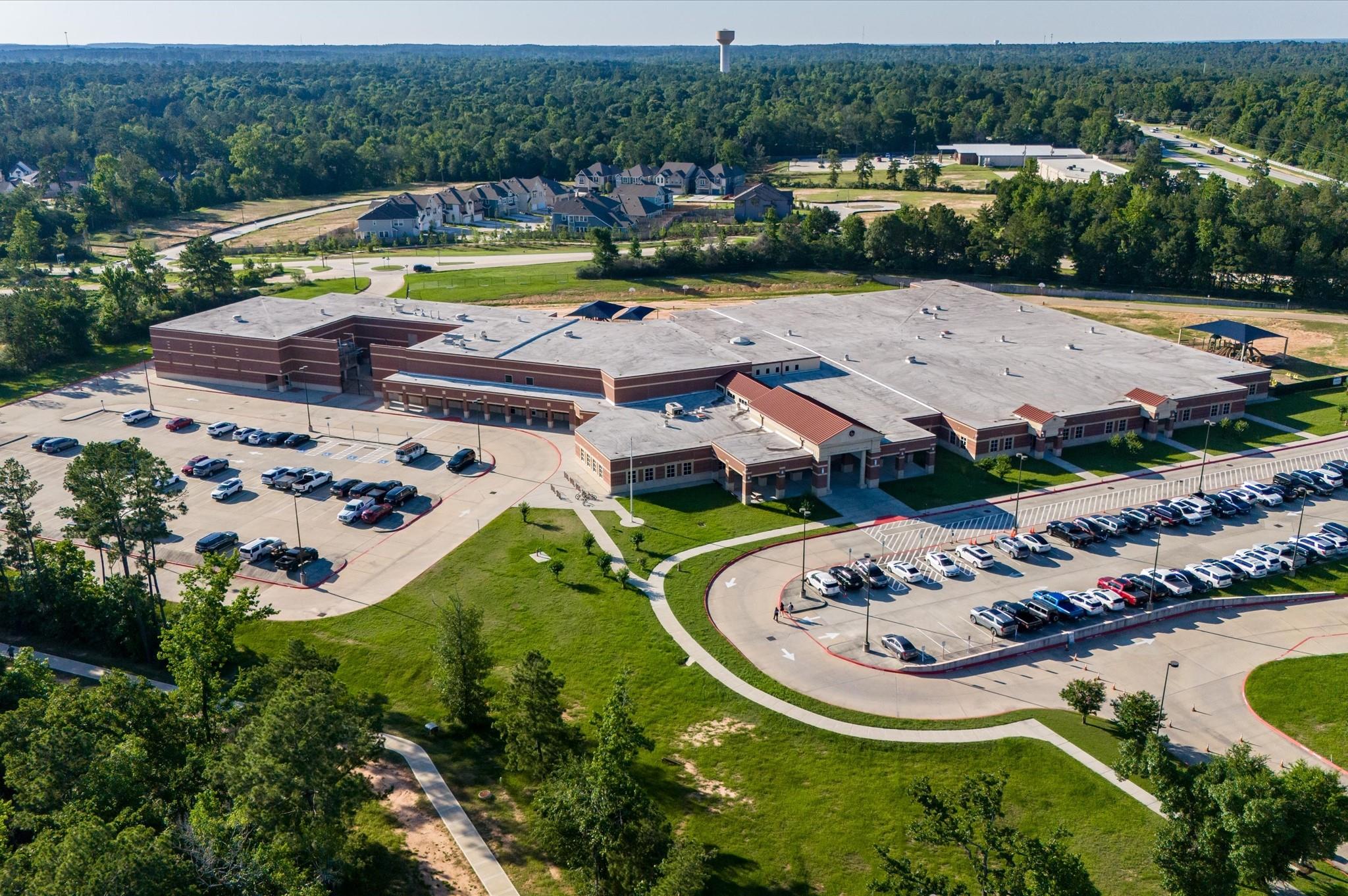 Large brick building with extensive parking lots and landscaped grounds, viewed from above.