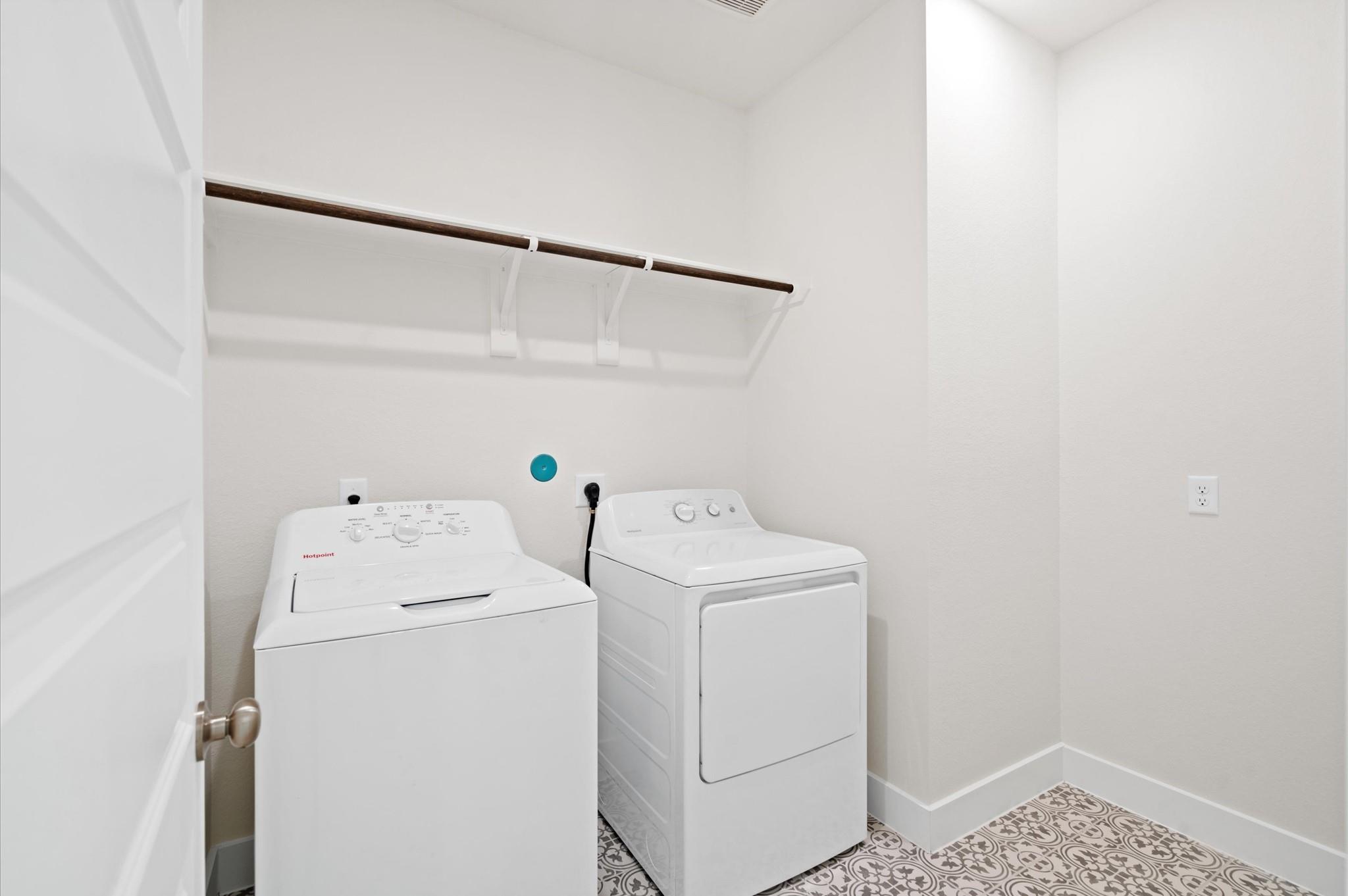 Laundry room with a white washer and dryer, hanging rod, and patterned tile floor.