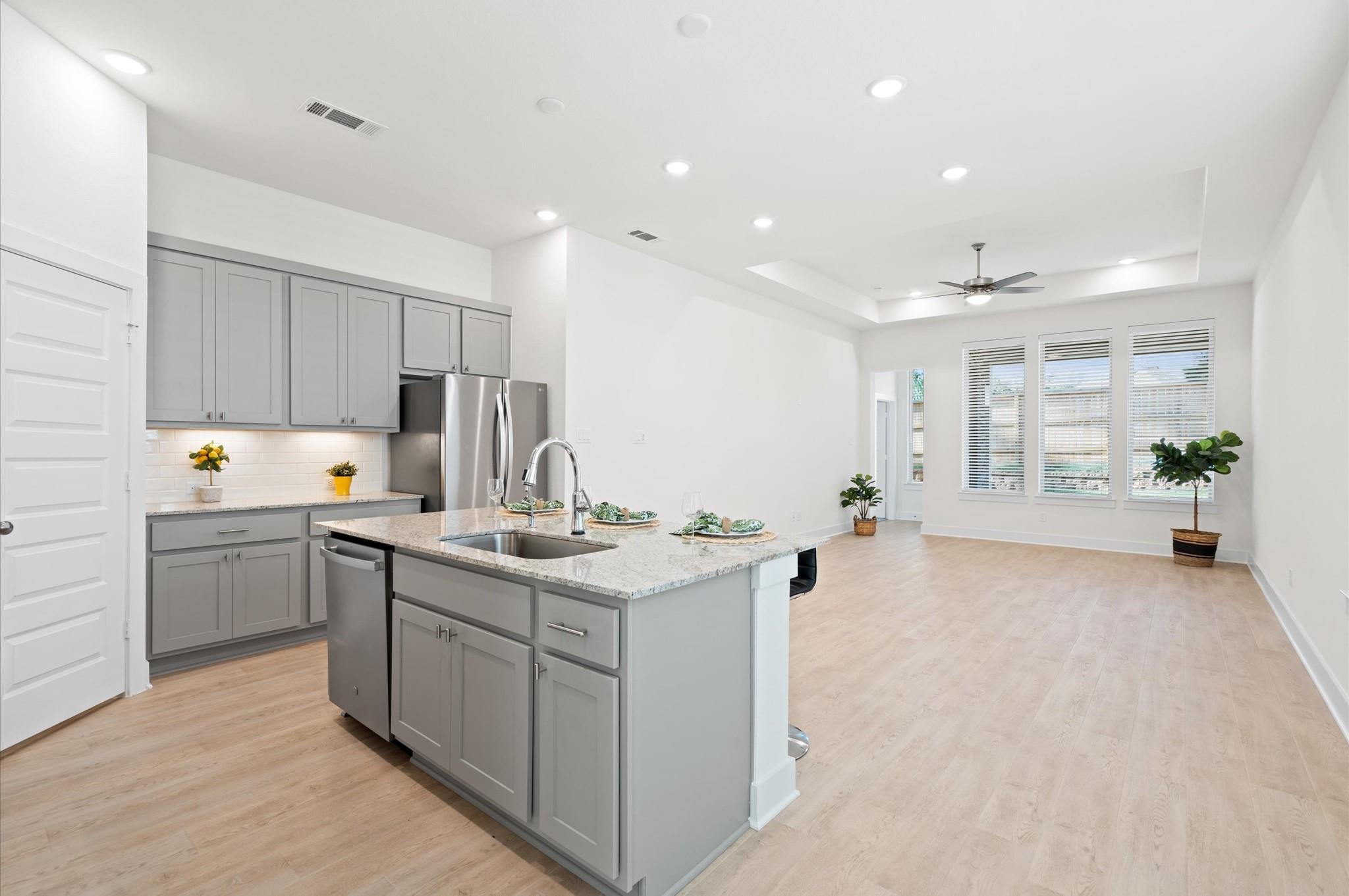 Open-plan kitchen with gray cabinets, stainless steel appliances, and a large granite island.