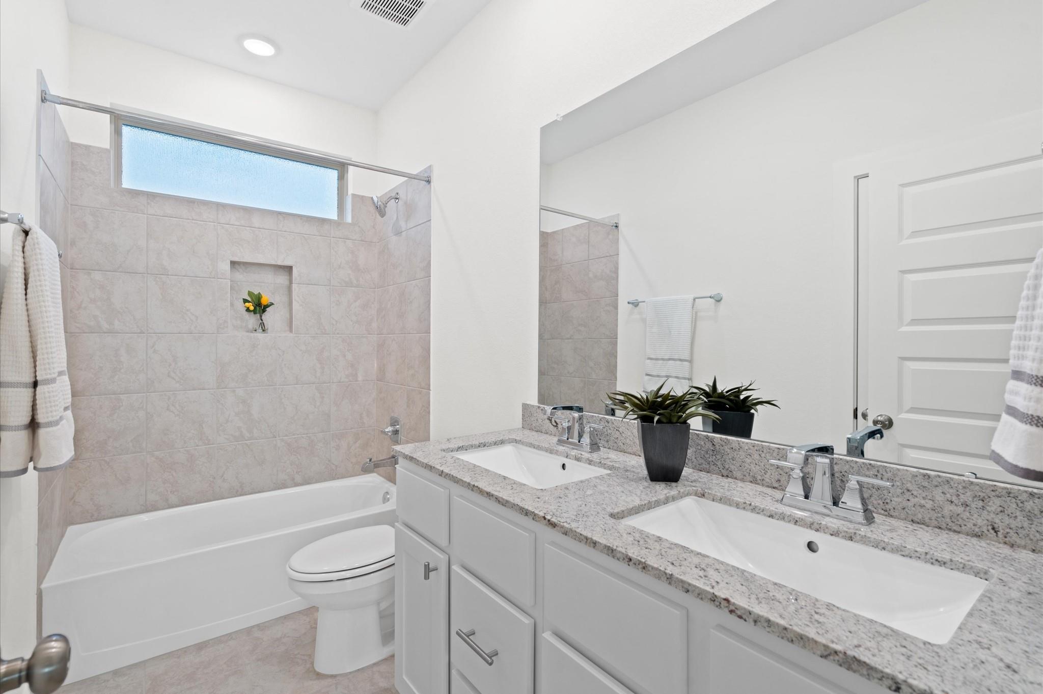 Bathroom with tiled tub and shower, frosted window, and double-sink granite vanity.