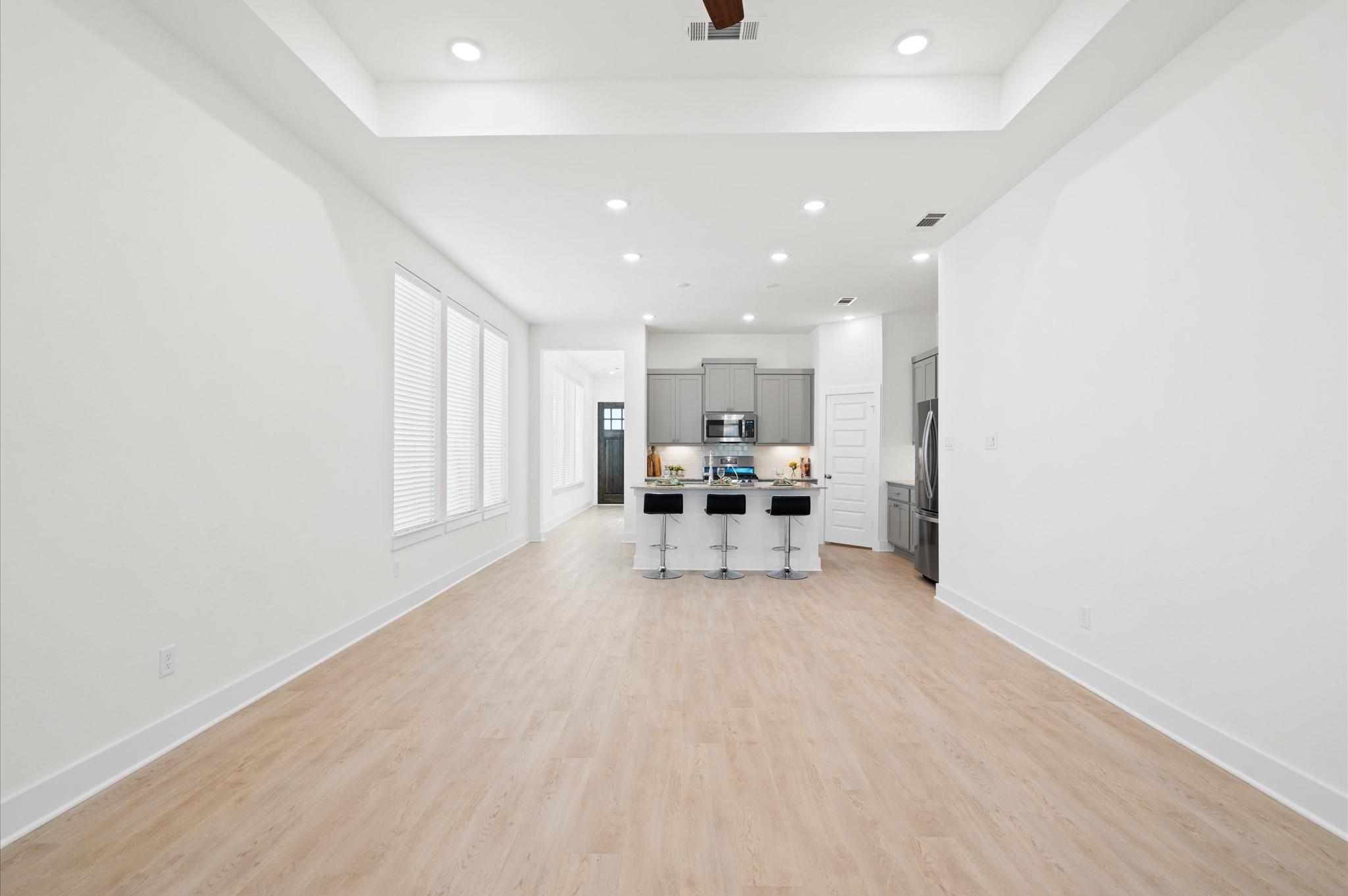 Open kitchen with gray cabinets, stainless appliances, and a white island with three black stools.