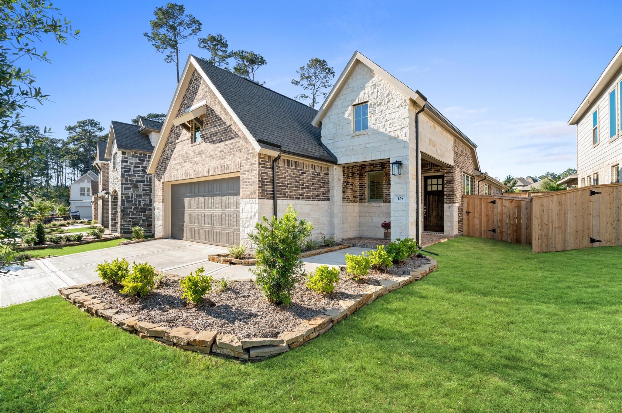 Stone-and-brick home with an attached garage, landscaped front garden, and fenced side yard.