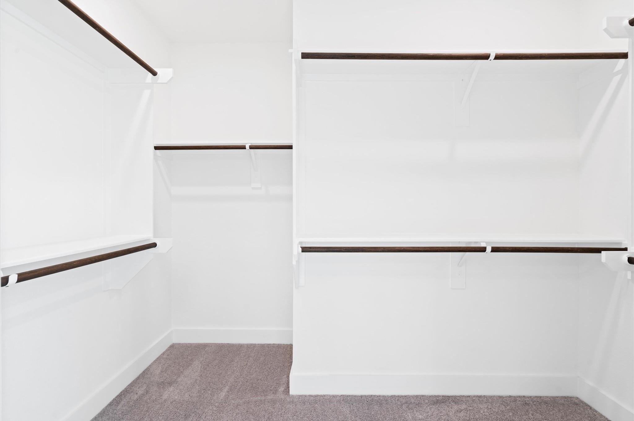 Empty walk-in closet with dark hanging rods and gray carpet.