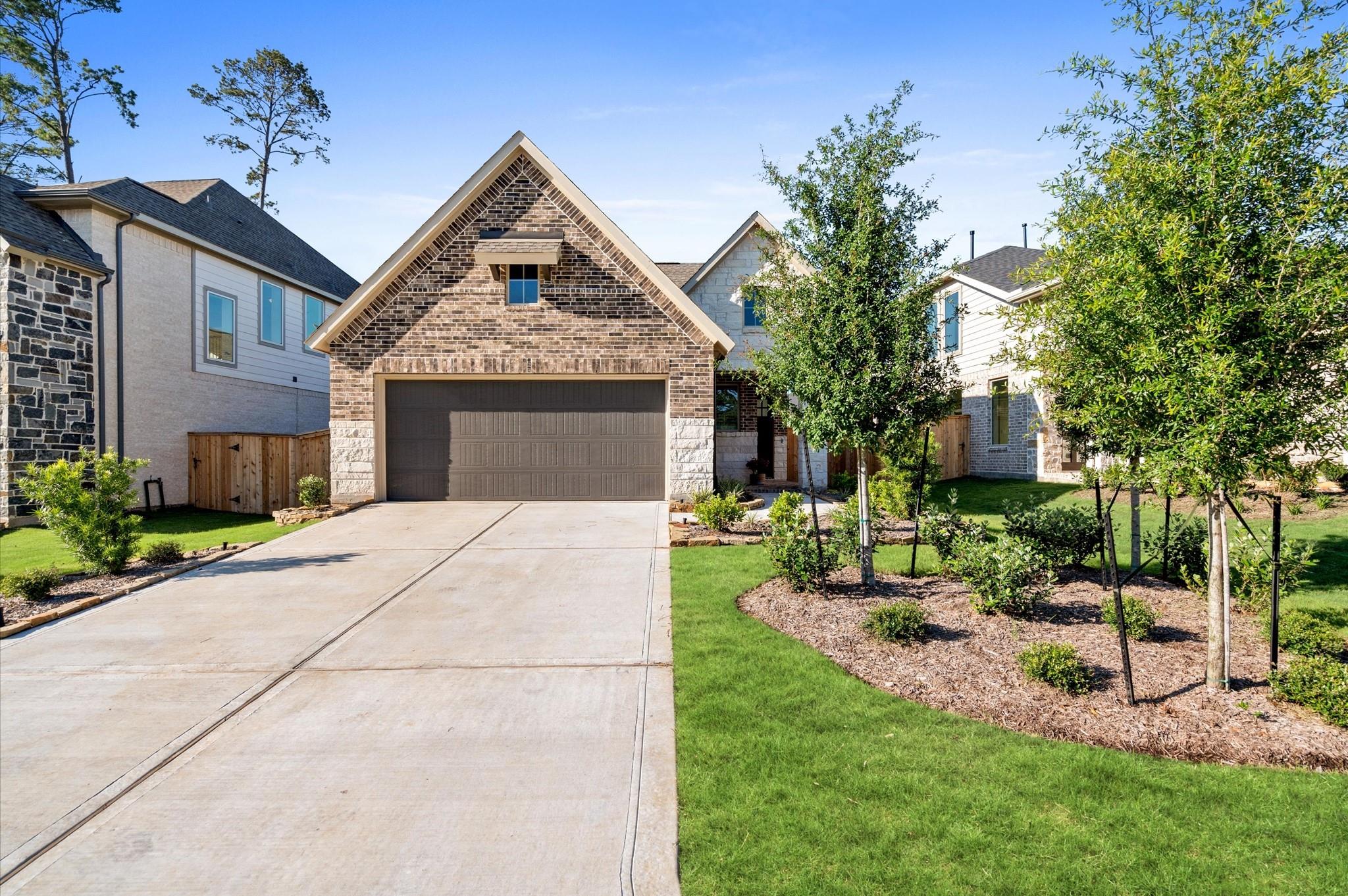 Two-story brick-and-stone home with a steep gable, wide garage, long driveway, and landscaped front yard.