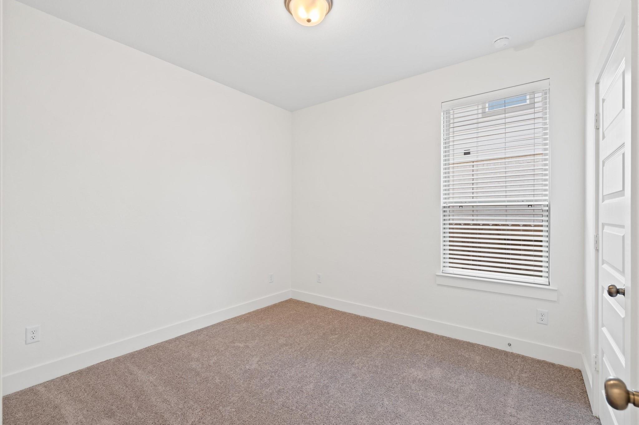 Empty bedroom with beige carpet, white walls, and a window with white blinds.