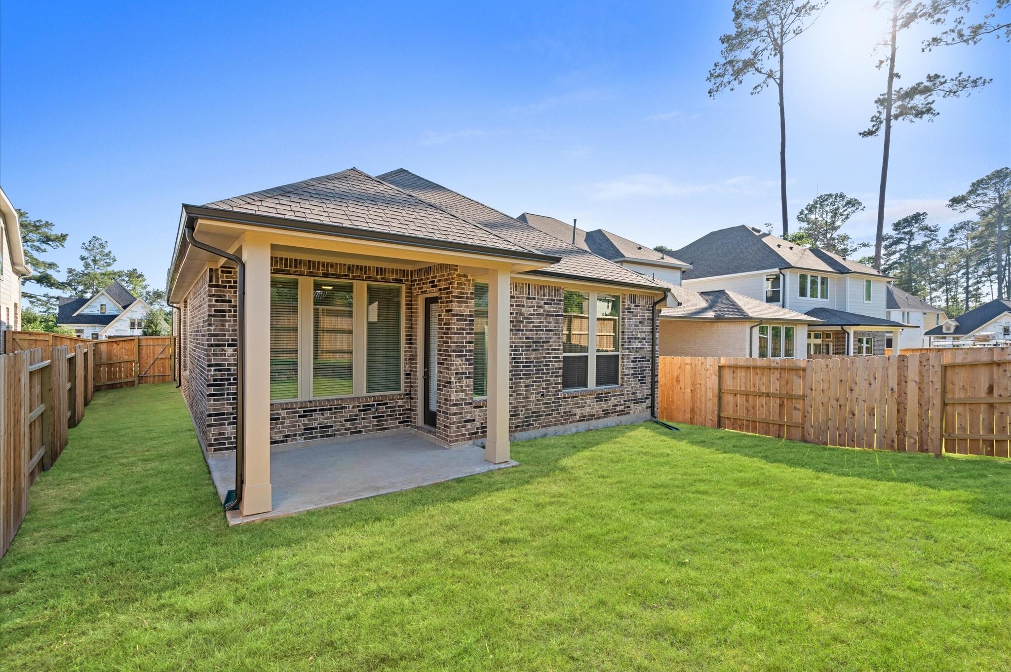 Brick home’s backyard with a covered patio, fenced lawn, and neighboring houses.