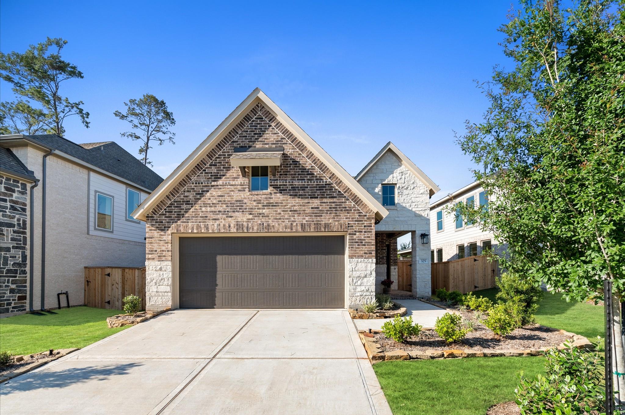 Two-story brick home with a double garage, landscaped front yard, and neighboring houses.