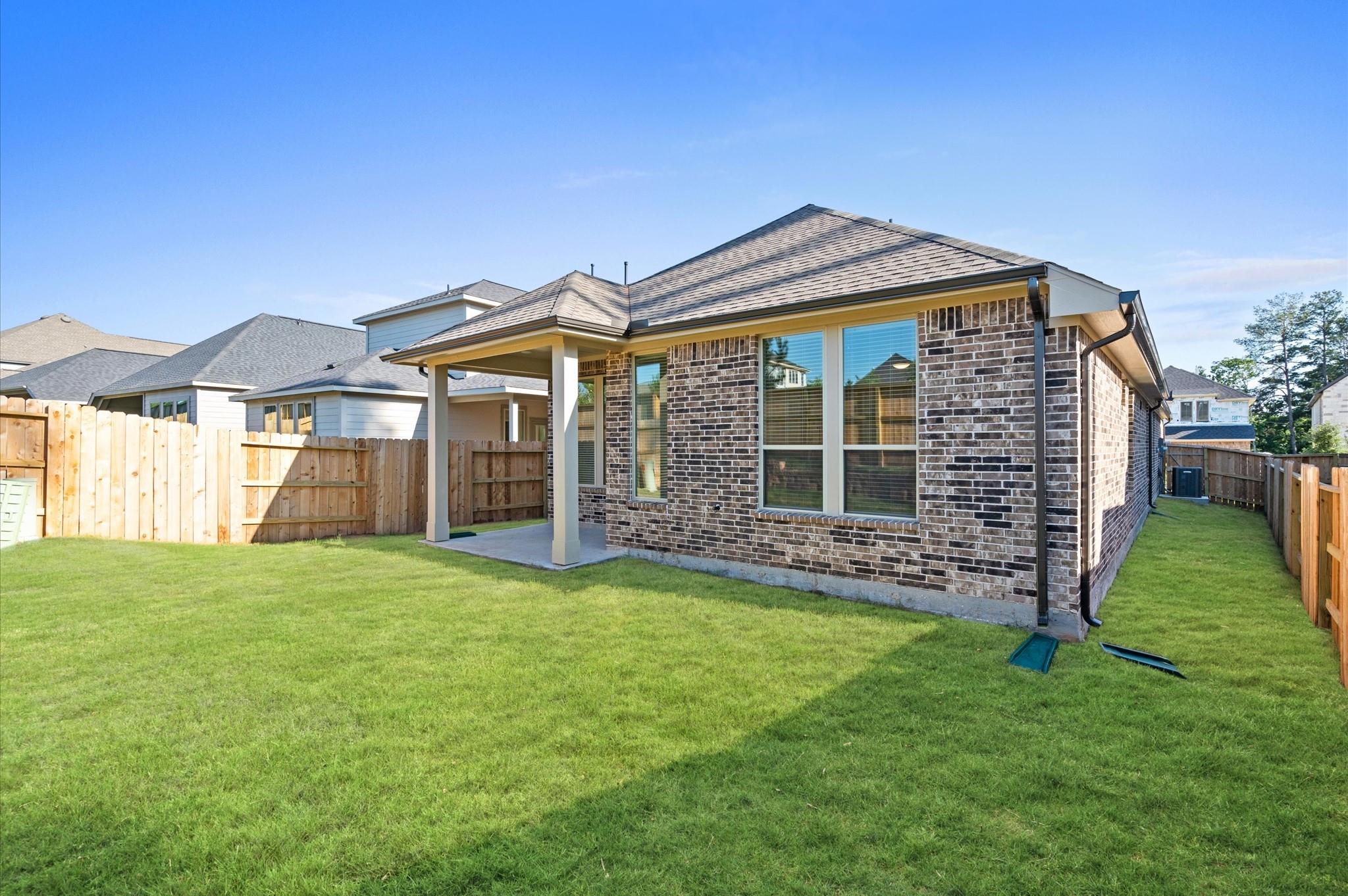 Rear brick exterior with covered patio and fenced lawn.