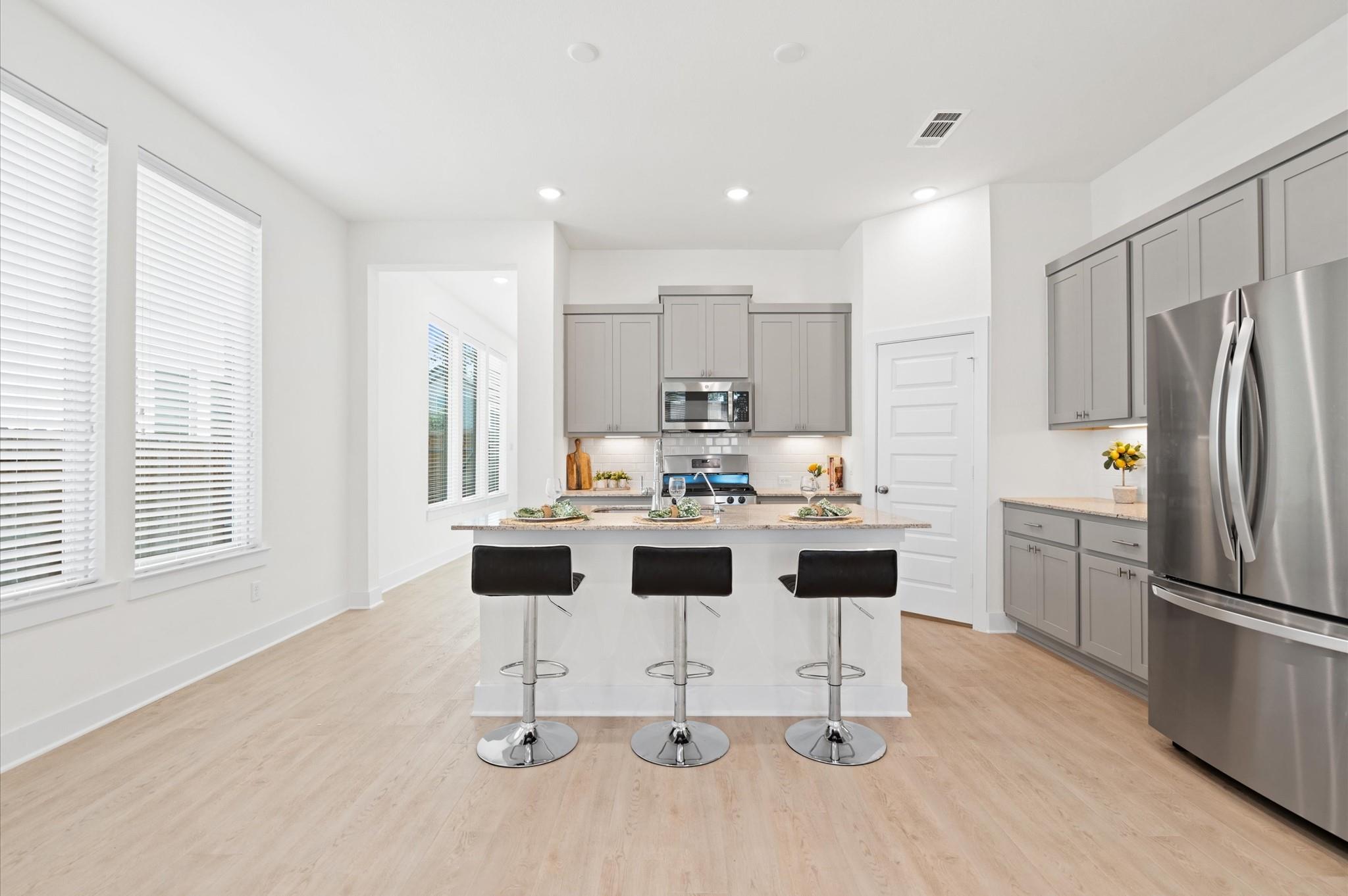 Bright kitchen with gray cabinets, stainless appliances, and an island with three black stools.